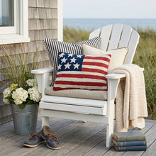 Load image into Gallery viewer, USA Flag Hook Pillow, rectangular hooked wool throw pillow featuring an American flag design displayed on a white Adirondack chair on a coastal cottage-style porch with striped and cream accent pillows and dune grass overlooking the water. 