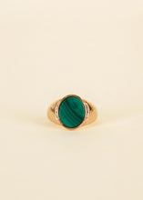 Load image into Gallery viewer, Gold Malachite Signet Rings, Front view of a 18K gold-plated signet ring with an oval emerald green malachite stone with dark diagonal banding against a cream background. 