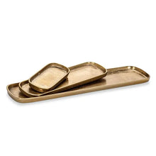 Load image into Gallery viewer, Gold Oval Tray, oval trays with a warm burnished gold finish, raised rims, and rounded corners, stacked to show three sizes, against a white background. 