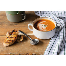 Load image into Gallery viewer, Danica Soup Bowls, lifestyle scene featuring an off-white stoneware bowl with side handles filled with tomato soup and a white cream swirl, arranged on a rustic wooden table next to toasted sliced bread, a metal spoon, and a checkered kitchen towel, with matching stacked stoneware soup bowls visible in the background. 