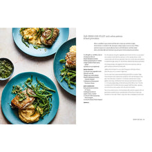 Load image into Gallery viewer, Mediterranean Summer Table Cookbook, open cookbook displaying a recipe spread with three blue plates of pan-fried cod fillets served with green vegetables and creamy polenta, a small blue bowl of green basil gremolata, alongside a recipe page on a white background.