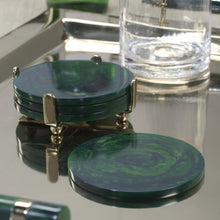 Load image into Gallery viewer, Set of round dark green resin coasters with a marbled pattern, stacked in a gold-tone metal holder with ball feet. One coaster placed in the front. Displayed on a reflective gold-tone tray next to a clear glass. 