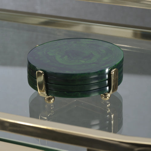 Set of four dark green resin coasters with a marble design stacked in a gold-tone metal holder with ball feet. On a reflective surface with a gold border. 