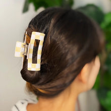 Load image into Gallery viewer, Checker Lovers Hair Claw | 5 Styles, rectangular white and yellow  checkerboard hair claw clip with a open cutout center securing a twisted updo, shown in dark brown hair with soft greenery in the background.  