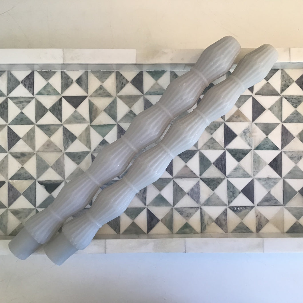 Two gray taper candles in a stacked diamond shape lying on a blue and white tray. 