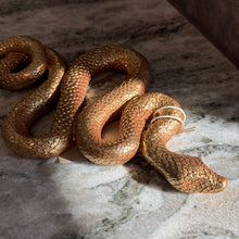 Load image into Gallery viewer, Gold Resin Snake Wall Décor, close-up of a gold snake with detailed textured scales and a tapered head, arranged in loose S-shaped curves on a mottled light gray and cream marble surface. 
