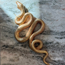 Load image into Gallery viewer, Gold Resin Snake Wall Décor, overhead view of a gold snake with detailed textured scales, tapered head, and a winding S-shaped body with a curled tail on a mottled gray and cream marble surface. 
