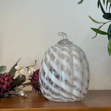 Load image into Gallery viewer, White Swirl Glass Pumpkin, tall clear glass pumpkin featuring white spiral stripes, textured ribbing, and a clear curved glass stem, displayed on a wooden surface with burgundy and white floral decor and greenery against a white background. 