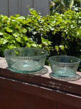 Load image into Gallery viewer, Two green glass embossed bowls on a wooden railing with green bushes in the background.