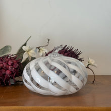 Load image into Gallery viewer, White Swirl Glass Pumpkins, short and wide clear glass pumpkin featuring white spiral stripes, textured ribbing, and a clear curved glass stem, displayed on a wooden surface with burgundy and white floral decor and greenery against a white background. 
