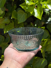 Load image into Gallery viewer, Hand holding a decorative green glass bowl with embossed patterns against a green leafy background.