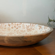 Load image into Gallery viewer, Cream Foliage Shallow Bowl, lifestyle image showing a close-up side view of the shallow mango wood bowl with visible natural wood grain, a cream enamel-coated interior, and tan leafy branch patterns, resting on a wooden table.