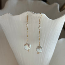 Load image into Gallery viewer, Freshwater Pearl Drop Earrings, close-up front view of 14k gold-filled earrings with gold-tone curved ear wires, a small white freshwater pearl near the top, and a delicate chain ending in a larger flattened, irregular freshwater pearl, hanging from a white ridged display with an uneven top edge.