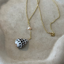 Load image into Gallery viewer, Freshwater Pearl &amp; Spotted Shell Necklace, view from above of a 14k gold-filled chain arranged on a beige textured tray, showing its clasp, a small peach-toned freshwater pearl, and a short chain drop ending in a white cone shell with dark brown spots.