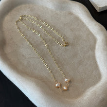 Load image into Gallery viewer, Coral Freshwater Pearl Necklace, overhead view of a 14k gold-filled chain arranged on a beige tray with a wavy rim, showing its clasp and three rounded, irregular freshwater pearls in peach and pale coral tones joined by wire-wrapped loops at the center.