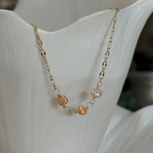 Load image into Gallery viewer, Coral Freshwater Pearl Necklace, close-up view of a 14k gold-filled chain with three rounded, irregular freshwater pearls in peach and pale coral tones, showing their lustrous surfaces and wire-wrapped connecting loops against a white ridged display.