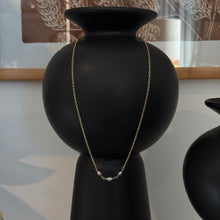 Load image into Gallery viewer, Lavender Freshwater Pearl Necklace, lifestyle image of a delicate 14k gold-filled chain with three oval lavender and silvery freshwater pearls at the center, displayed around a tall black vase with framed botanical artwork in the background.