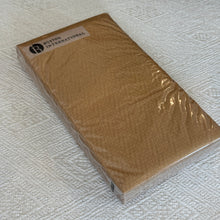 Load image into Gallery viewer, Gold Herringbone Textured Guest Towel, view from above at an angle of rectangular gold-colored paper guest towels with a subtle herringbone texture, wrapped in clear packaging with a rectangular white Boston International label near the top, resting on cream fabric with a woven geometric pattern.