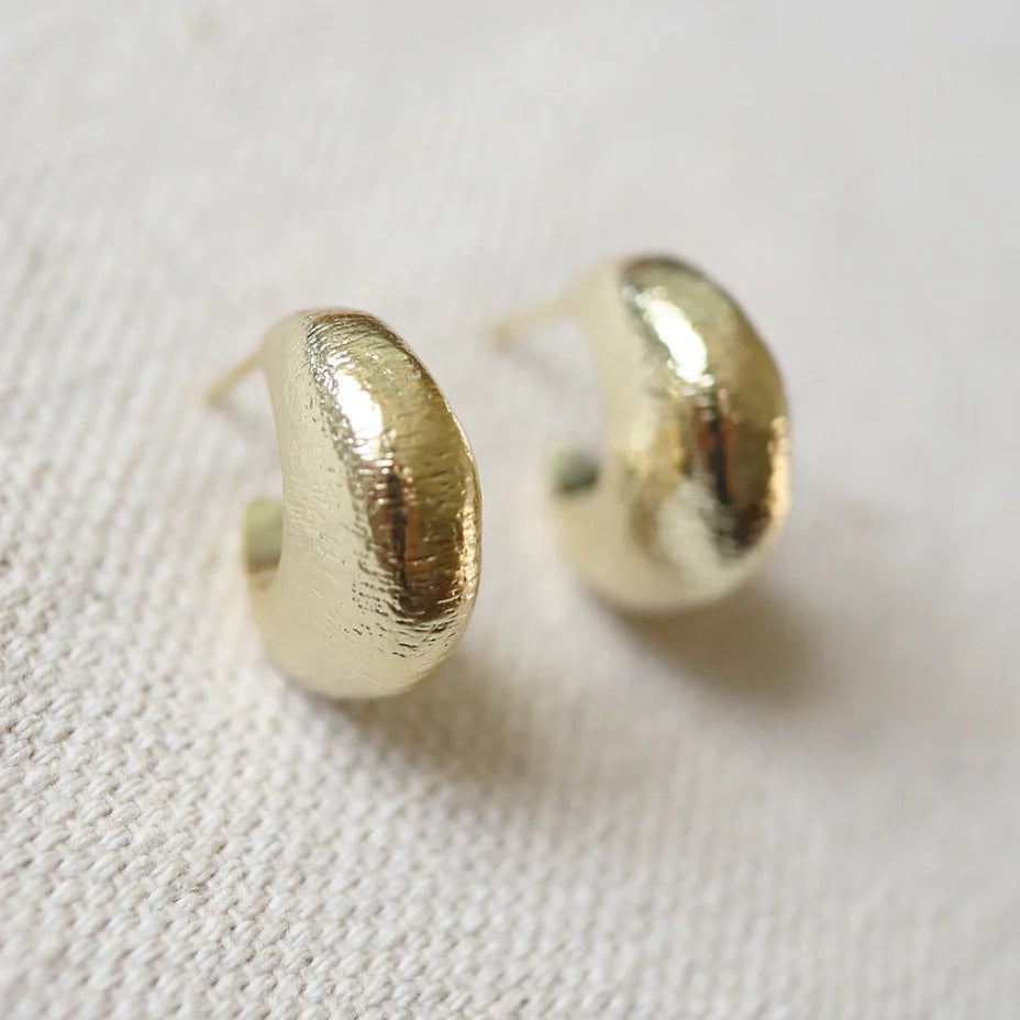 14K gold semi-matte double plated brass casting hoop earrings with sterling silver posts on a cream woven fabric surface.