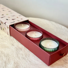 Load image into Gallery viewer, Three unlit white candles in decorative ribbed glass holders inside a red box on a white fur surface. A white colored  box cover ,with blurred colorful decorations slid out from behind the red box. Pink, red, and green glass candle holders. Against a white background. 