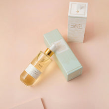 Load image into Gallery viewer, Lollia Snowdrop dry body oil displayed beside its two-part packaging, featuring a mint patterned bottom box and a white patterned top box, resting against a soft pink background.