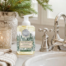 Load image into Gallery viewer, Evergreen Foaming Hand Wash, lifestyle image of a clear rectangular plastic bottle filled with pale yellow soap and topped with a white foaming pump, featuring a silver-colored embossed seal and an illustrated green evergreen tree label with a cream “Evergreen” panel, displayed beside a polished silver-colored faucet, folded cream towels, a lit candle, and a vase of evergreen branches.