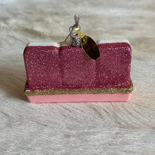 Load image into Gallery viewer, Mahjong Tiles Ornament, lifestyle back view showing three joined tile shapes covered in dusty rose pink glitter above a pink rack with gold glitter trim, topped with a silver-colored cap and hanging cord, displayed on a cream fur-textured surface.