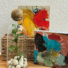 Load image into Gallery viewer, Glass Decanter/ Two Sizes, clear glass decanter topped with a mango wood sphere stopper and filled with decorative white stones and green stem, displayed beside two colorful abstract artwork and a woven basket on a wood surface. 