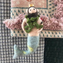 Load image into Gallery viewer, Felt Merman Ornament, wool felt merman ornament with a gold crown, dark beard and hair, green seaweed boa, and gray tail accented with yellow, displayed on patterned textiles.  
